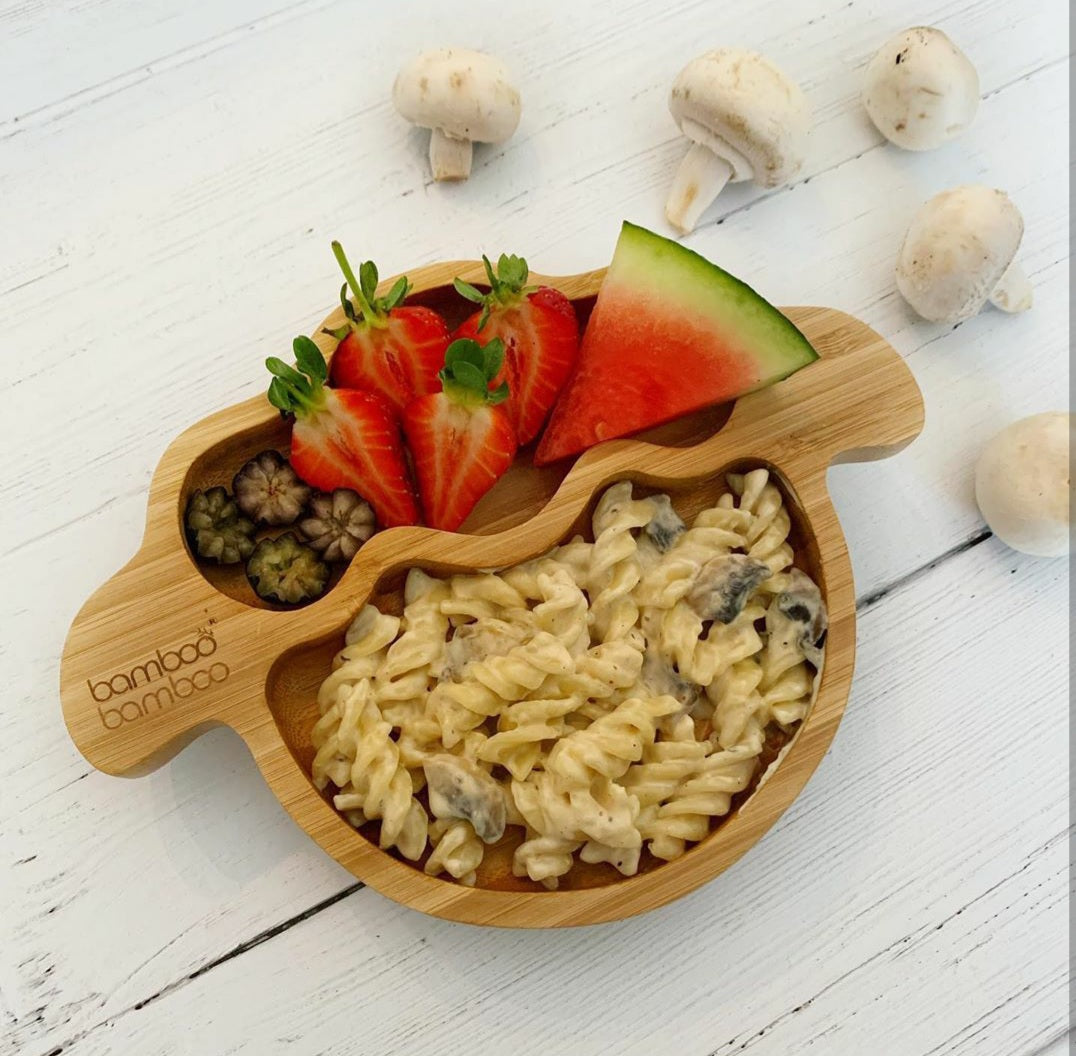 Creamy mushroom pasta with strawberries and watermelon on a bamboo plate.