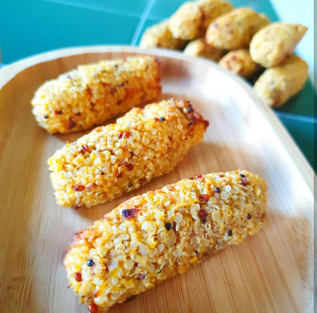Three golden quinoa croquettes on a wooden platter, with more in the background.