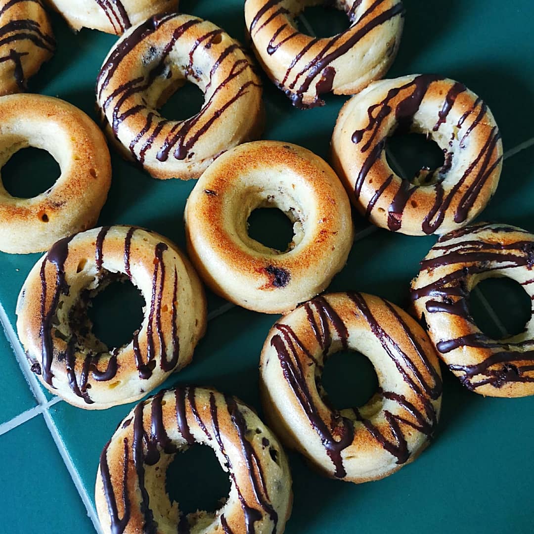 Baked doughnuts with chocolate drizzle on a green tiled surface.