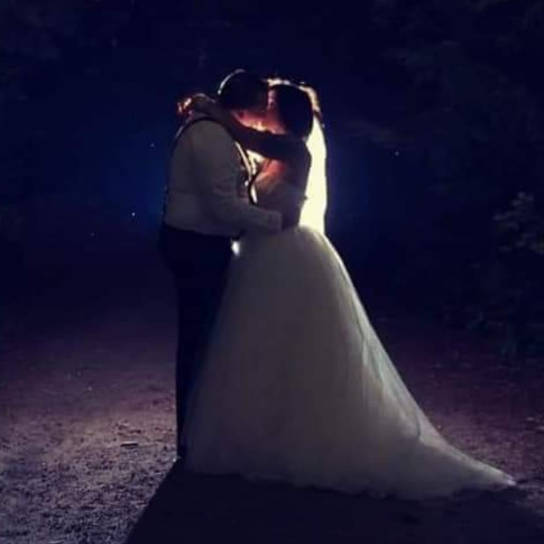 Silhouetted couple in wedding attire share a kiss, illuminated by a warm glow in a dark setting.