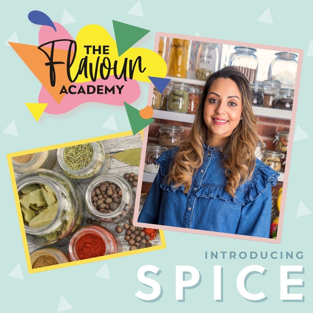 A smiling woman in a denim shirt with jars of spices, next to jars of dried herbs and peppercorns.