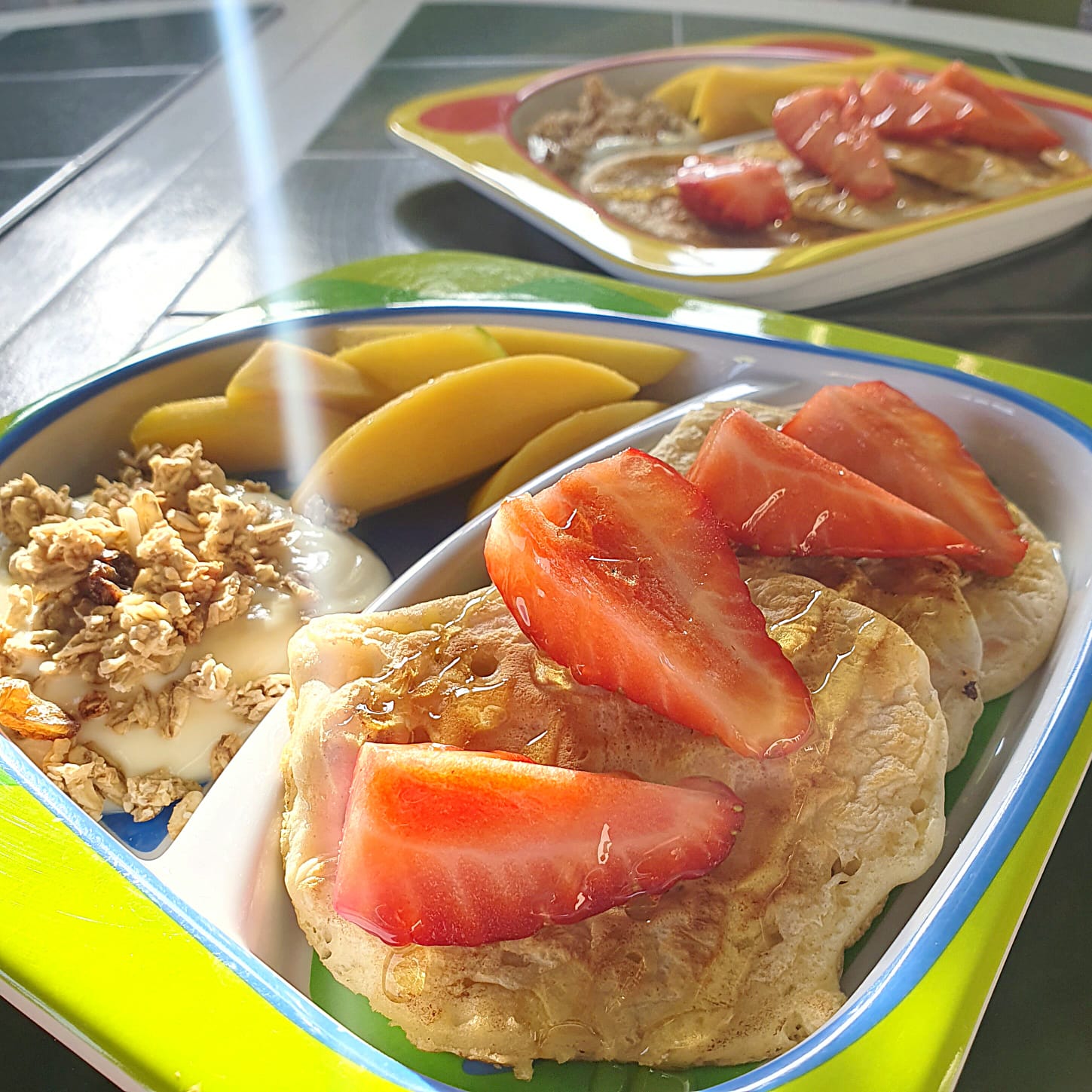 Fluffy eggless pancakes with fresh strawberries, mango slices, and granola with yoghurt on a colourful plate.