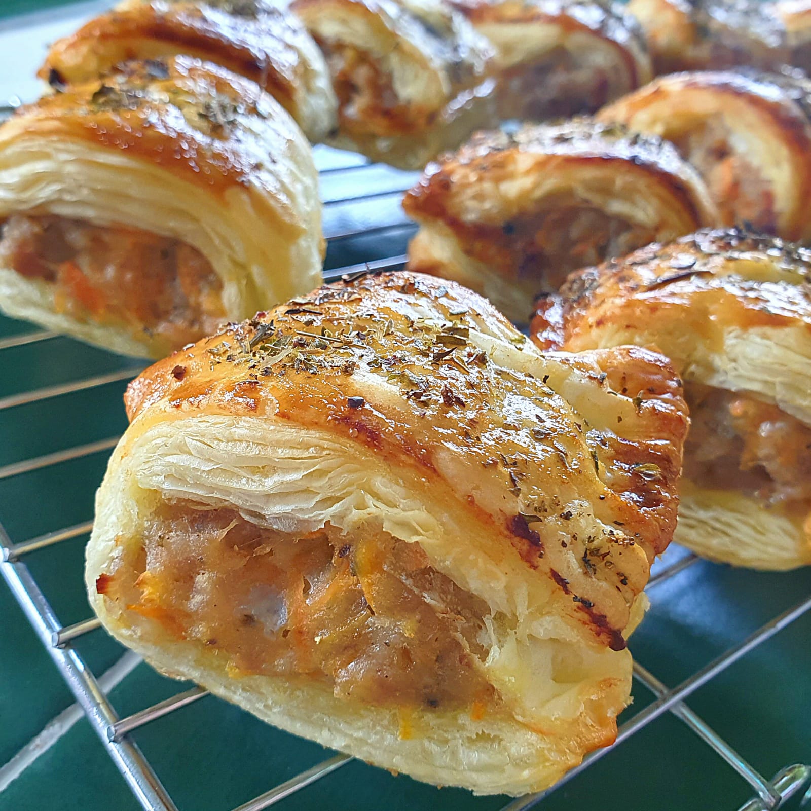 Golden, flaky carrot & apple sausage rolls cooling on a wire rack, sprinkled with herbs.