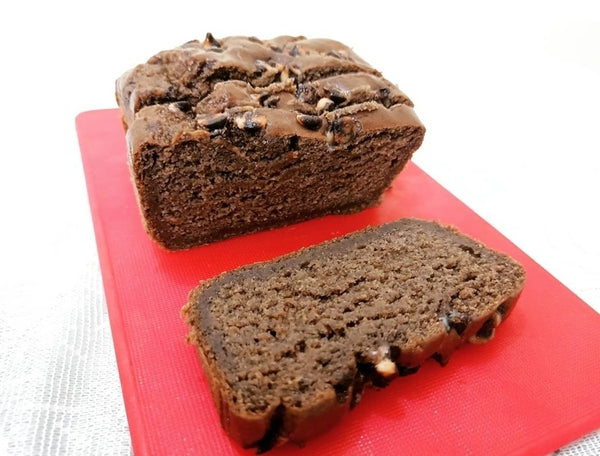 Sliced banana chocolate loaf cake with nuts on a red chopping board.
