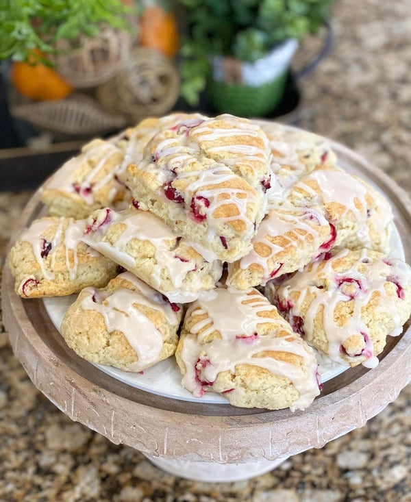 A wooden cake stand piled high with freshly baked cranberry scones, drizzled with white icing.