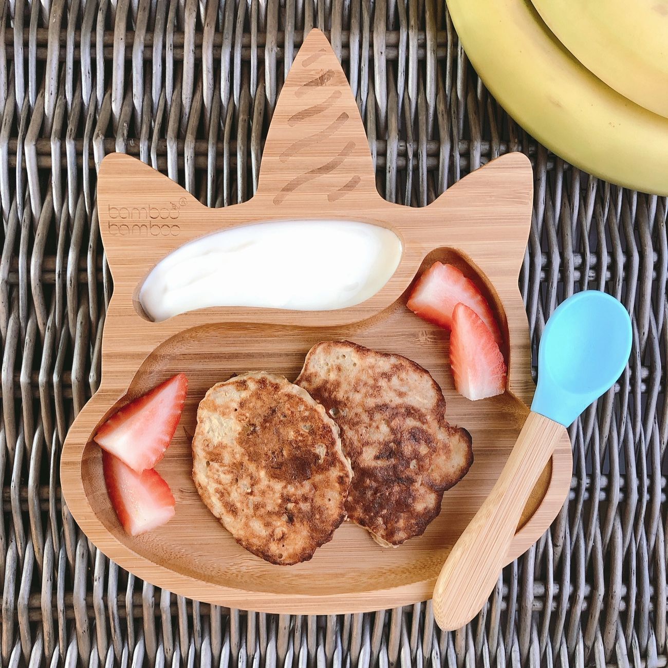 Two golden banana pancakes on a bamboo unicorn plate with yoghurt and strawberries.