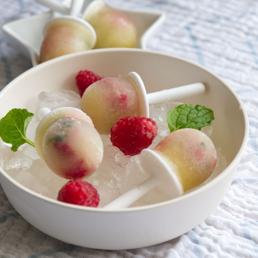 Pale yellow and pink chamomile & apple ice lollies with raspberries and mint on ice.