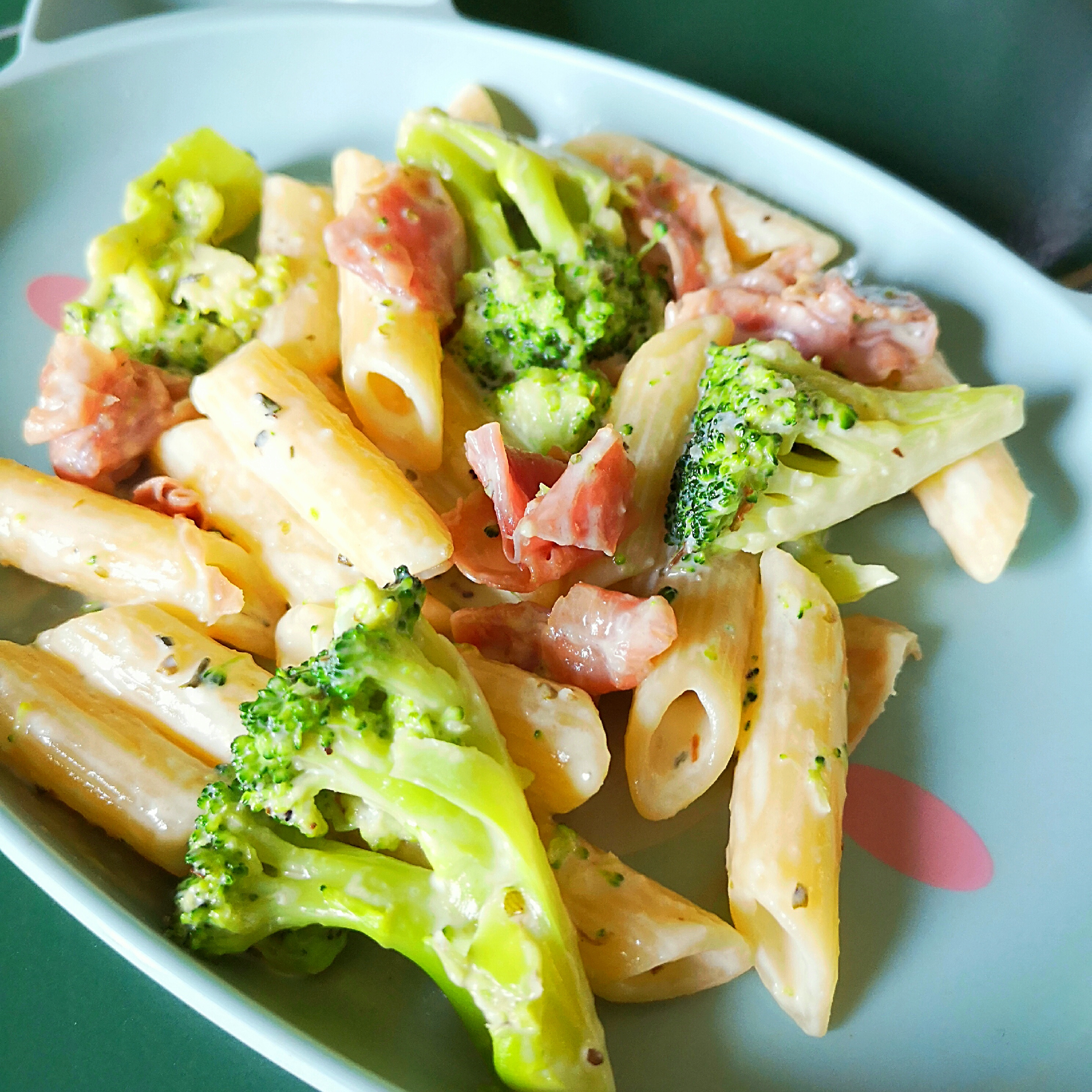 Creamy penne carbonara with crispy pancetta and vibrant green broccoli florets on a light blue plate.