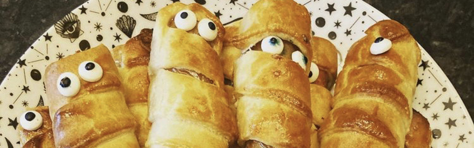 Golden-brown sausage mummies with candy eyes on a star-patterned plate.