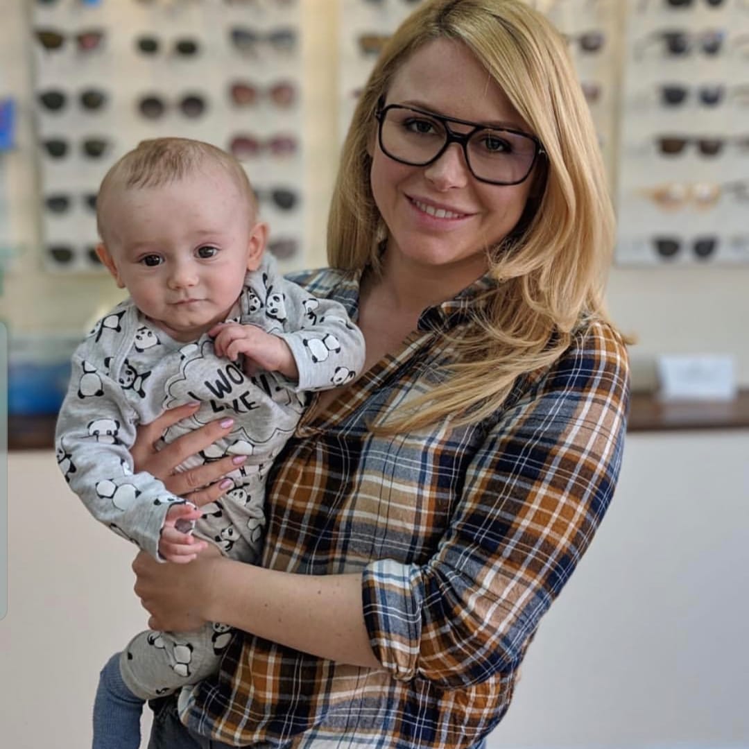 Blonde woman in glasses and plaid shirt holding a baby in a panda-print romper.