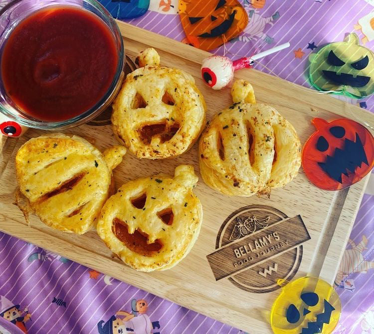 Golden, flaky pumpkin-shaped pizza pockets with a side of tomato dip, on a Halloween-themed mat.