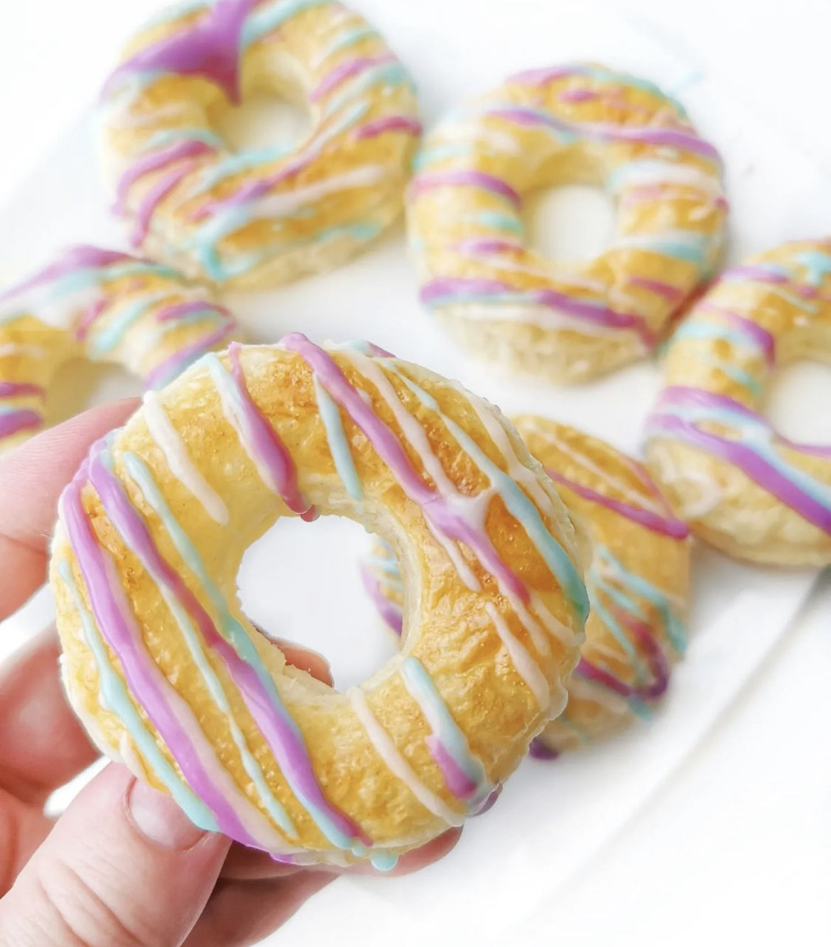 Golden air fryer donuts with colourful purple, blue, and white icing drizzle.
