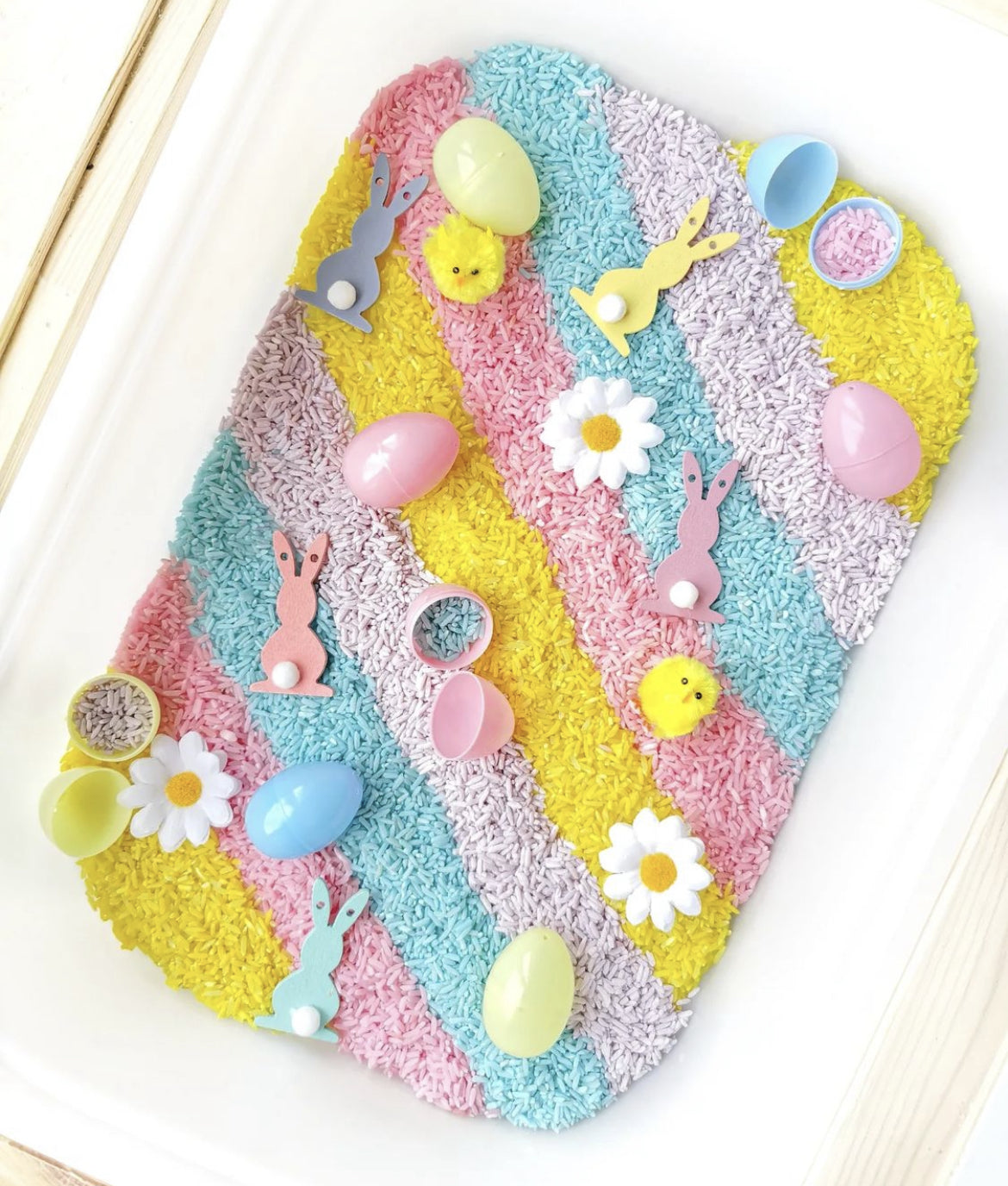 Colourful rainbow rice sensory bin with Easter eggs, bunnies, and chicks.