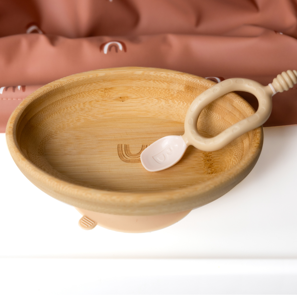 Natural bamboo suction bowl with curved sides and a beige silicone spoon, on a white surface. - Product image