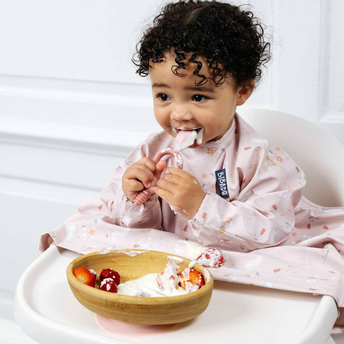 Happy baby in a pink floral bib eating yogurt and berries from a natural bamboo suction bowl. - Product image