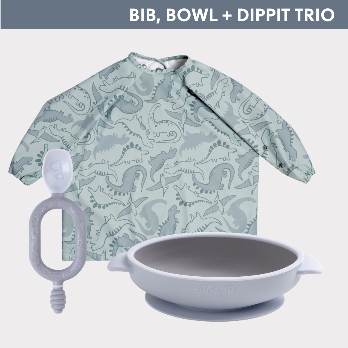 Light green long-sleeved weaning bib with dinosaur print, grey silicone suction bowl, and grey Dippit spoon. - Product image