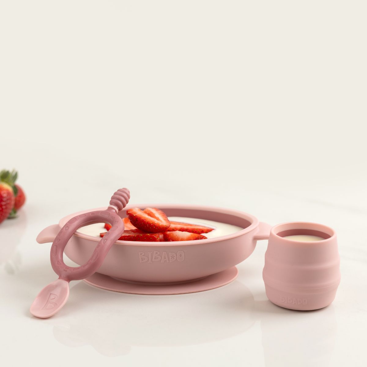 Pink silicone suction bowl with strawberries, matching training cup, and baby spoon. - Product image