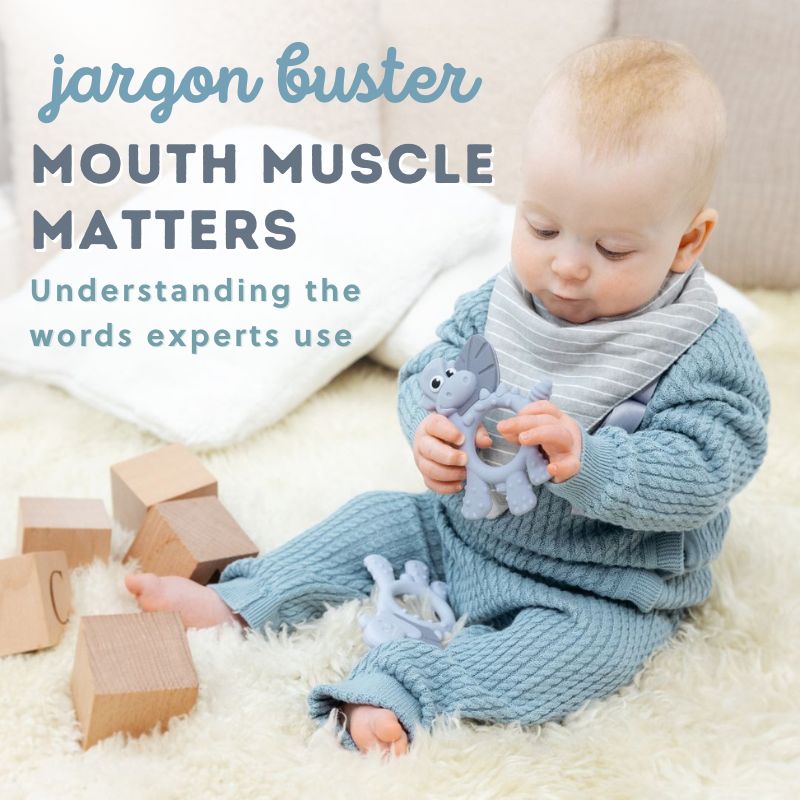 Baby in blue knit outfit holding a grey elephant teether, sitting on a fluffy rug with wooden blocks.