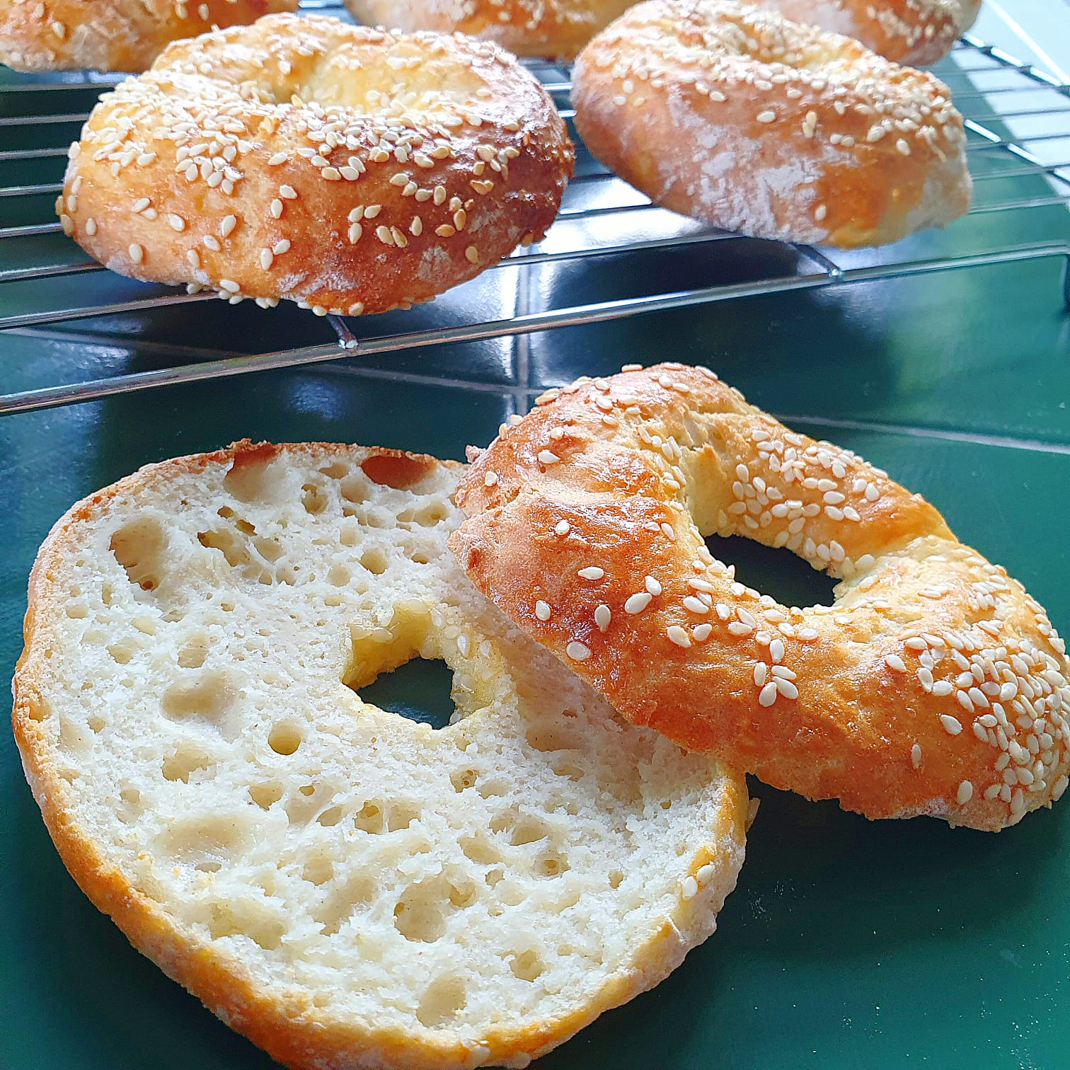 Freshly baked, sesame-topped 2-ingredient bagels cooling on a wire rack, one sliced open.