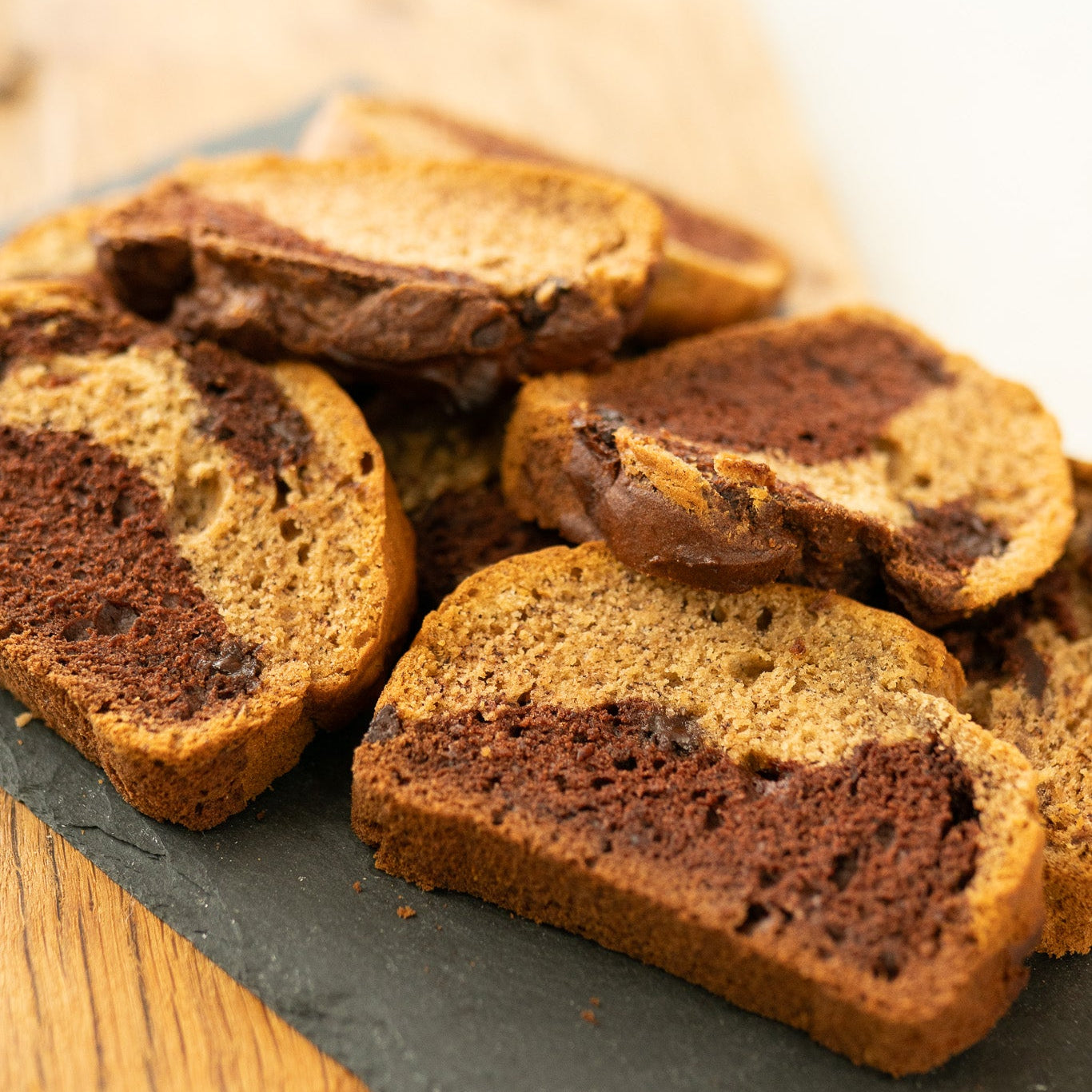 Slices of marbled banana bread with light and dark brown swirls on a dark slate.