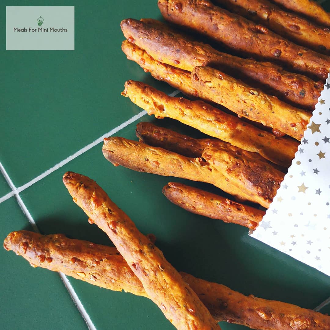 Golden Italian herb breadsticks spilling from a star-patterned bag onto a green surface.