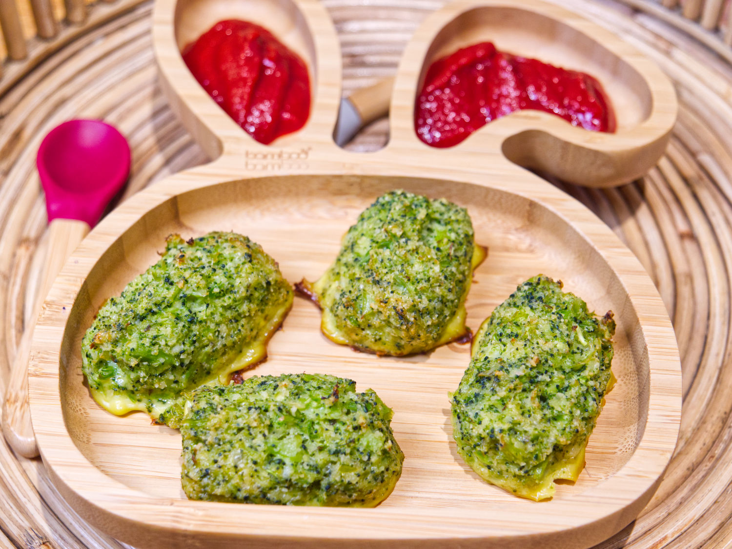 Four golden-brown broccoli tots on a bamboo bunny plate with two portions of tomato ketchup.