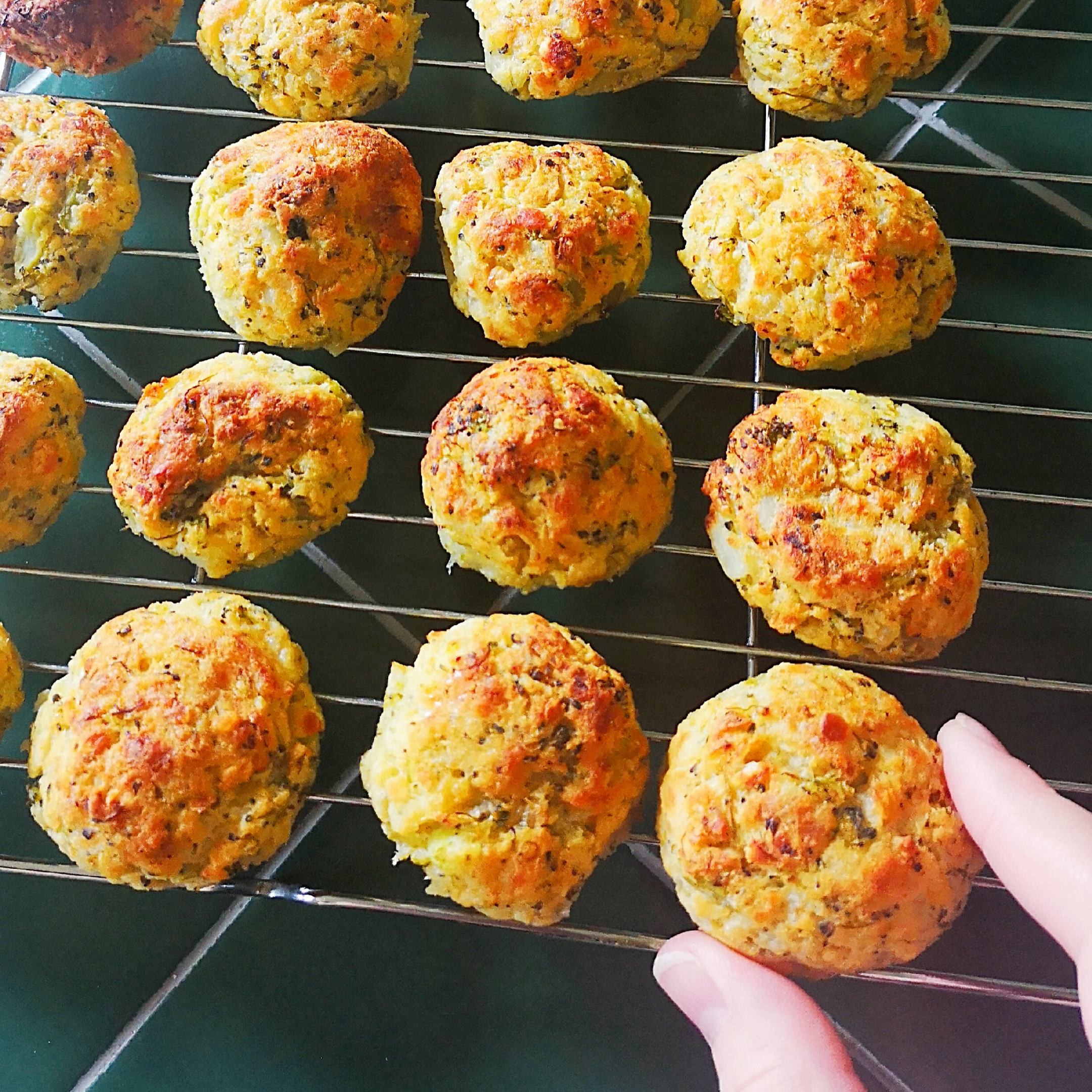 Golden-brown broccoli & lentil bites cooling on a wire rack, with a hand reaching for one.