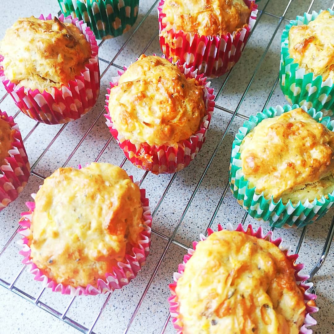 Golden cheesy carrot muffins in colourful red and green paper cases on a cooling rack.