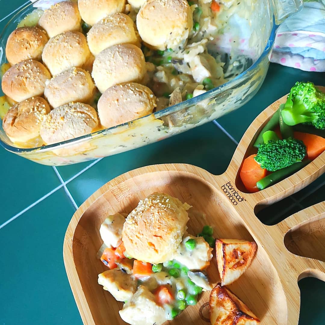 Creamy chicken cobbler in a glass dish and a child's bamboo plate with vegetables.