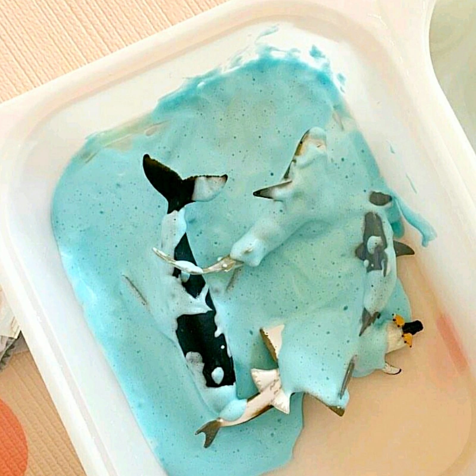 Toy whales and sharks submerged in light blue edible foam in a white tray.