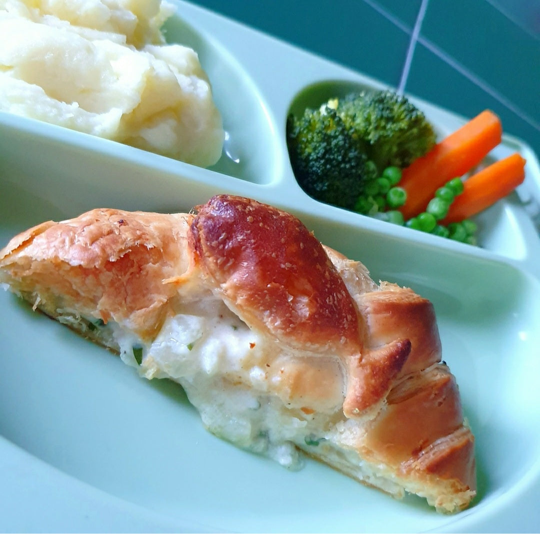 Golden puff pastry "Under the Sea Pie" with creamy filling, served with mashed potato, broccoli, and carrots.