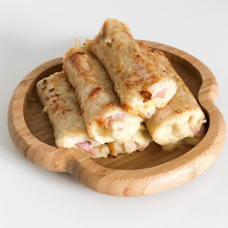 Golden-brown savoury French roll-ups with melted cheese and ham, served on a wooden plate.