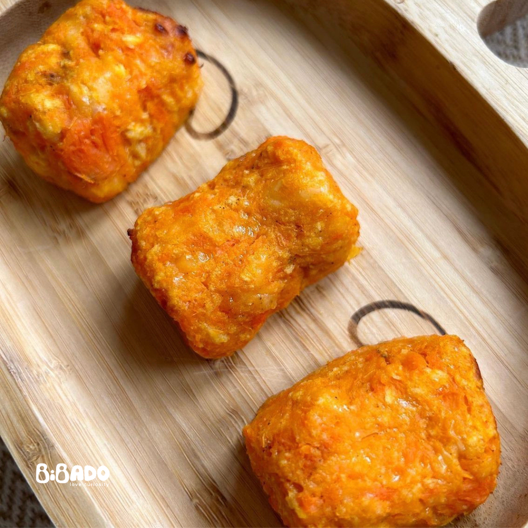 Three vibrant orange cheesy carrot and sweet potato tots on a wooden tray.