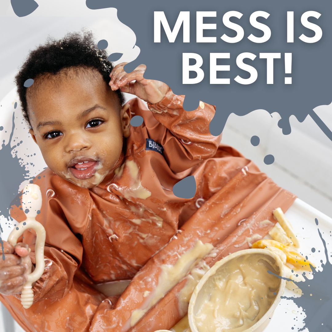 Happy baby in a brown long-sleeved bib, covered in messy food, enjoying independent weaning.