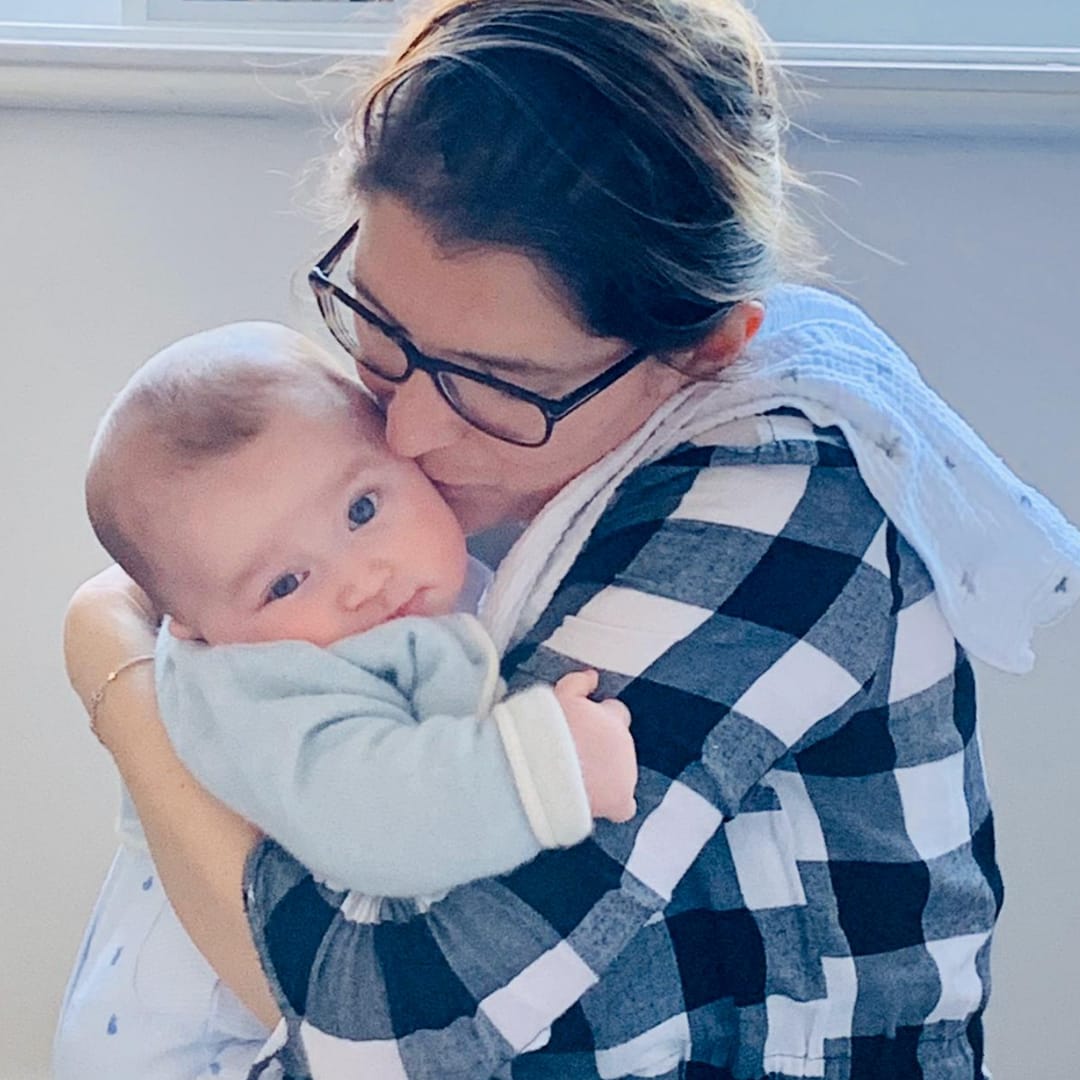 Woman in a black and white checked shirt kissing a baby in a light blue top.