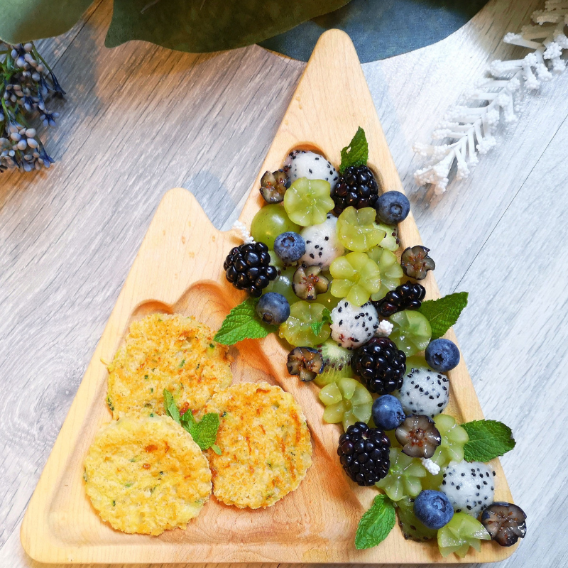 Golden courgette pancakes with a colourful fruit salad on a mountain-shaped wooden plate.