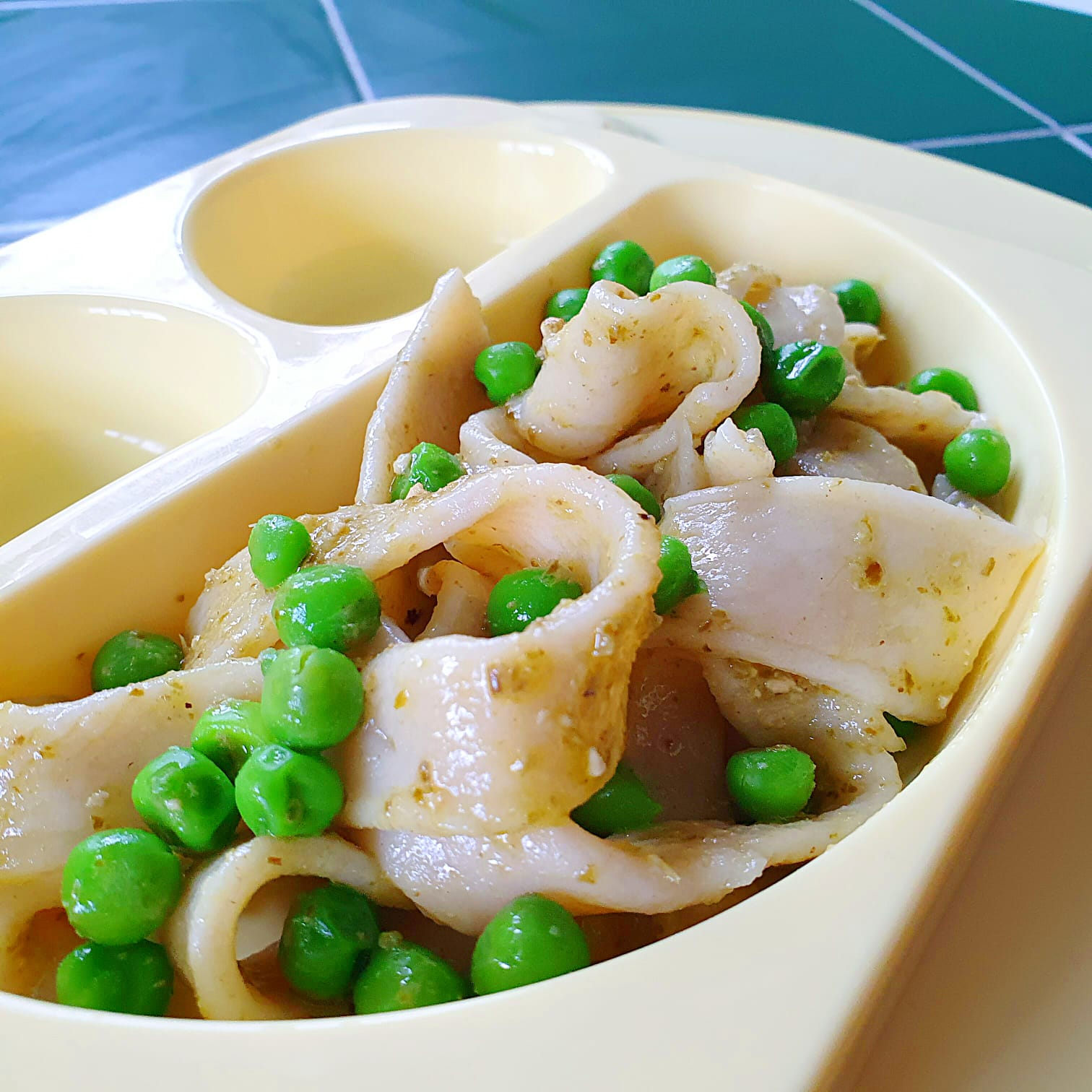 Simple 3-ingredient pasta with green peas served on a beige partitioned plate.