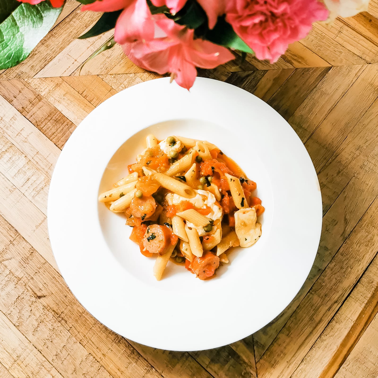 Penne Sicilian pasta with tomato sauce, sausage, peas, and mozzarella on a white plate.