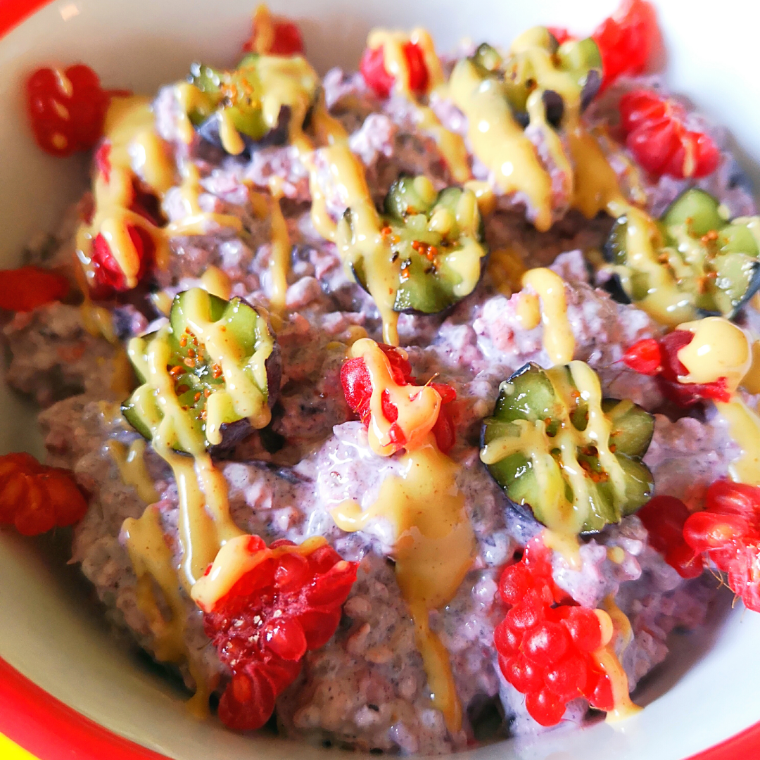Creamy berry breakfast pudding topped with fresh raspberries, kiwi flowers, and a drizzle of honey.