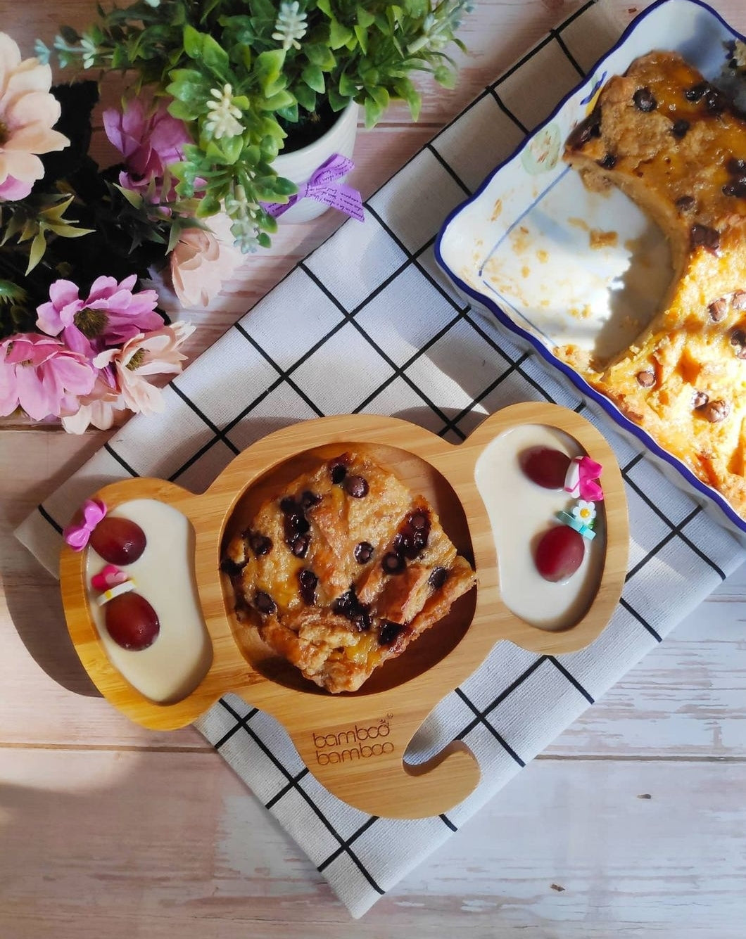 Warm banana bread pudding with chocolate chips, served on a bamboo plate with grapes and cream.