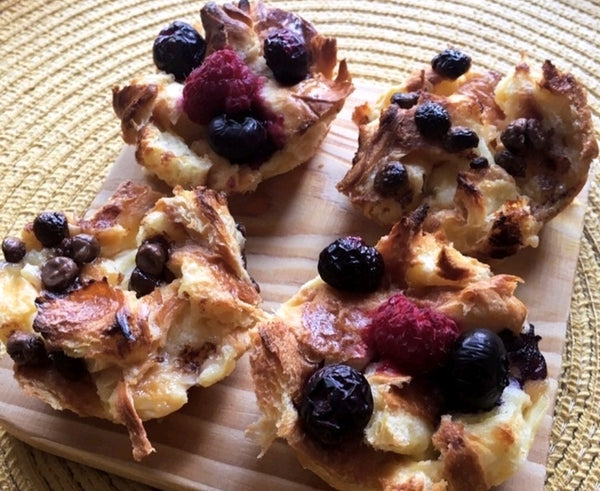Golden croissant French toast cups with blueberries and raspberries on a wooden board.