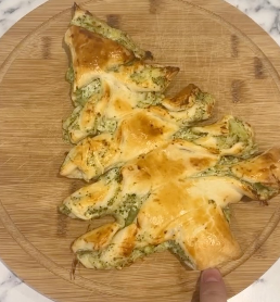 Golden-baked cream cheese and broccoli slice shaped like a Christmas tree on a wooden board.