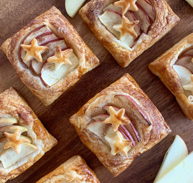 Golden apple and cinnamon pastries with star-shaped puff pastry on a wooden board.