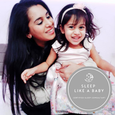 Smiling mother holding a happy toddler in a pink dress, promoting "Sleep Like A Baby".