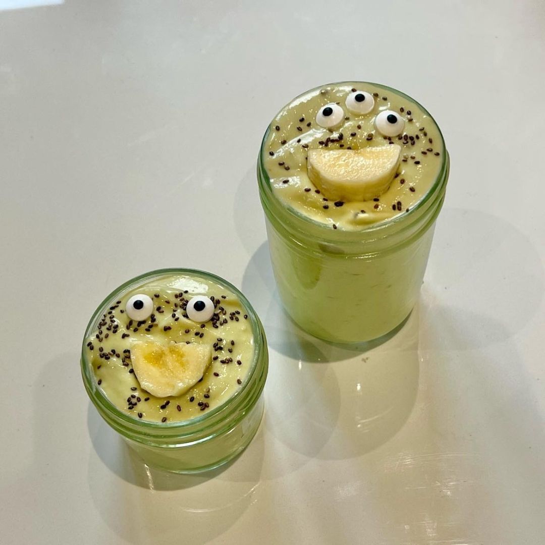 Two green monster smoothies with banana smiles and chia seed sprinkles in glass jars.