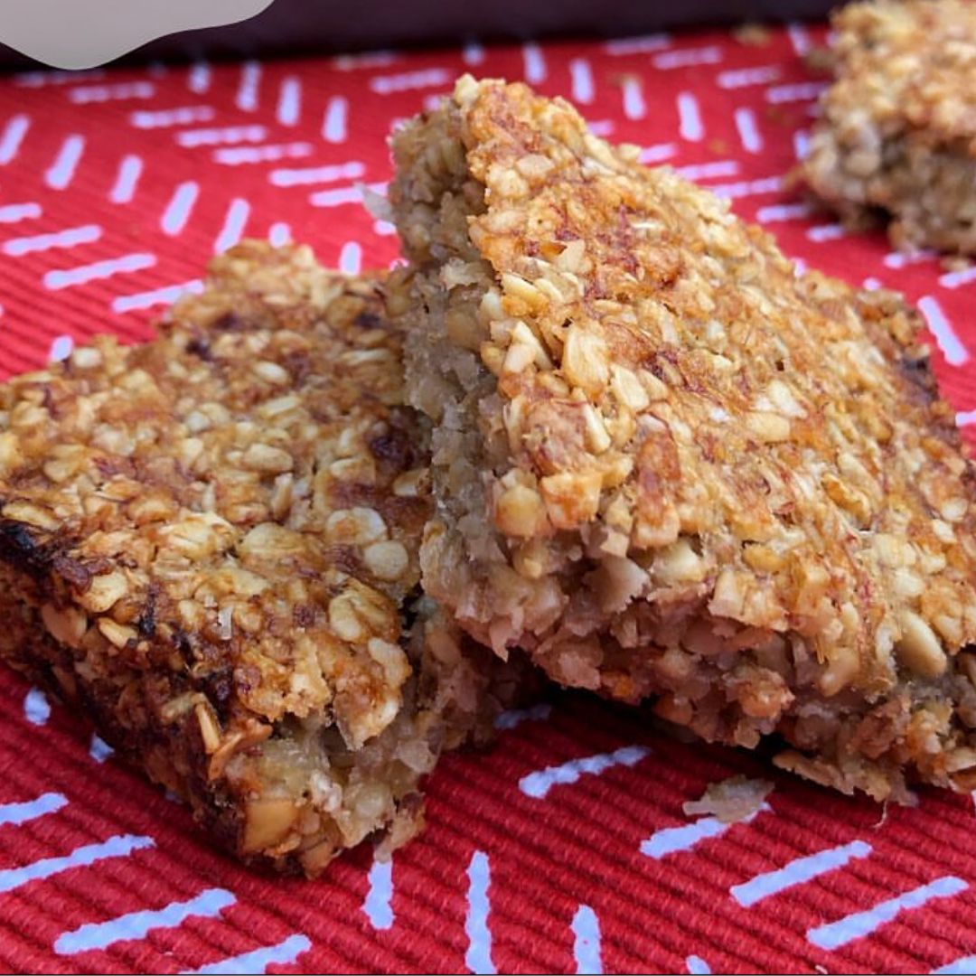 Two golden banana and coconut flapjacks on a red and white patterned cloth.