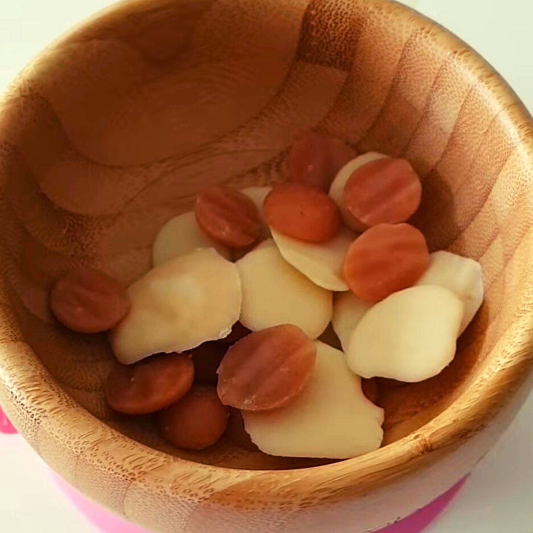 Close-up of a wooden bowl filled with light yellow and reddish-brown yoghurt drops.