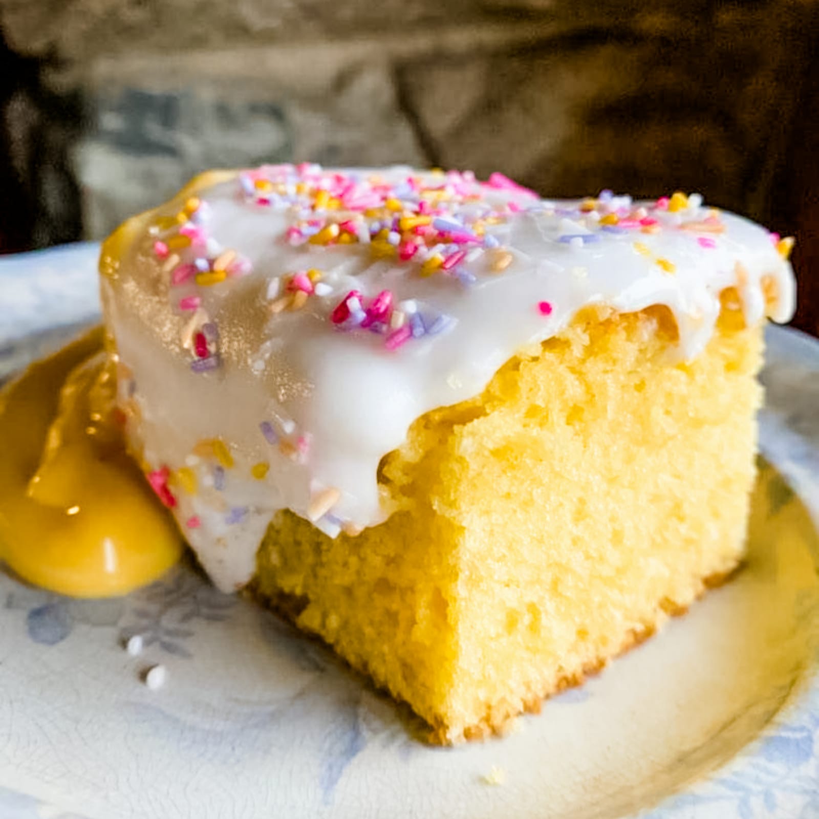 A slice of classic old school sponge cake with white icing and colourful sprinkles, served with custard.