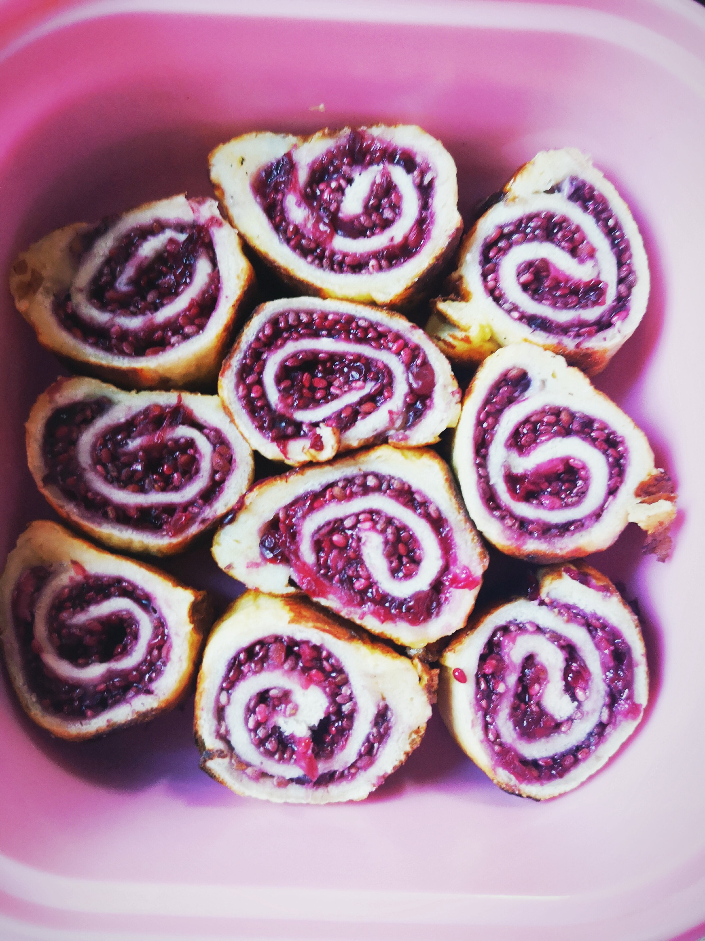 Swirly pancake bread rolls with a vibrant purple berry filling, presented in a pink dish.