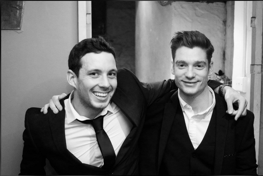 Two smiling men in suits with arms around each other, depicting friendship.